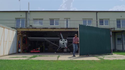 Mann öffnet Shutter Hangar mit Flugzeug und bereitet Privatflugzeug auf den Flug vor