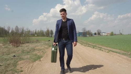Mann geht mit Treibstoffkanister auf einer staubigen Straße, seinem Auto geht der Treibstoff aus