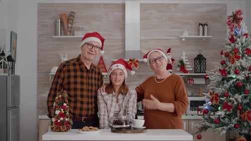 Family Wearing Santa Hats Waving in Kitchen