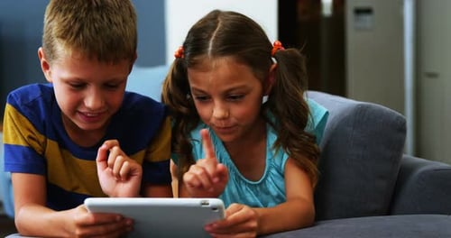 Two Children Using Tablet Together on Sofa