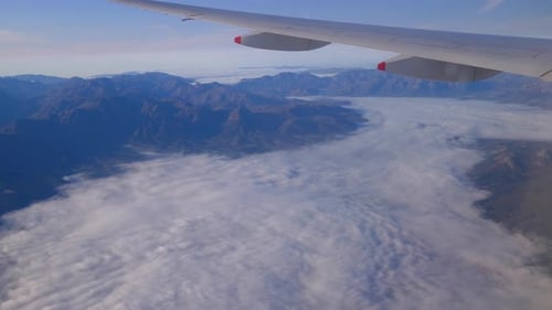 Luftaufnahme von Bergen und Fliegen über Wolken mit Blick auf den Flugzeugflügel.