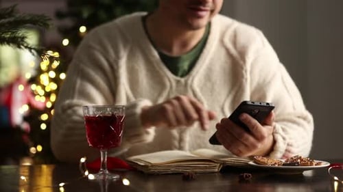 Man Using Phone at Table with Christmas Tree