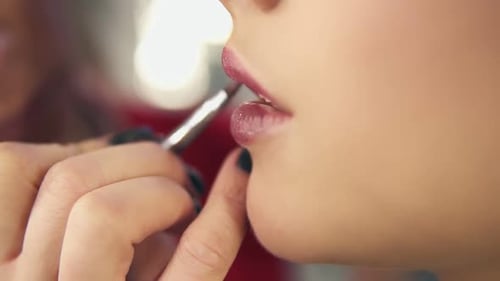 Nahaufnahme der Hand eines professionellen Visagisten, der einen speziellen Pinsel verwendet, um Lippenstift auf die Models aufzutragen
