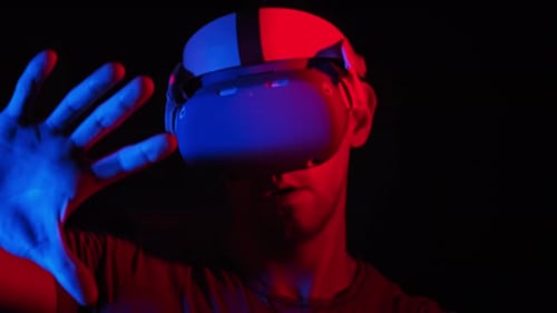 Jovem joga um jogo em um capacete VR sob luz vermelha/azul