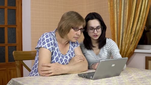 Daughter Teaches Mother How To Use a Laptop. A Young Woman Shows Her Old Mother Where To Click on a