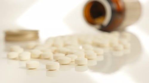 Pills Spilled from Medicine Bottle on White Surface