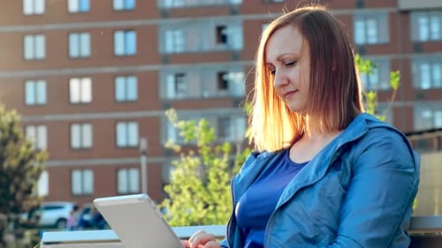 Woman Using Tablet Computer Sitting on Bench in City