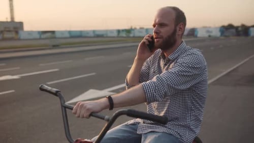 Young Man with Bmx Bicycle Uses His Phone at Sunset on the Street
