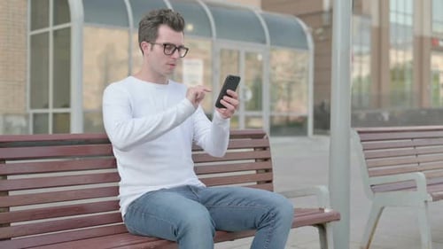 Young Man Using Smartphone While Sitting on Bench