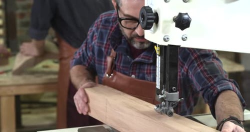 Man Cuts Wood with Band Saw in Workshop