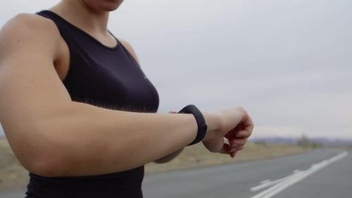 Frau in Sportbekleidung misst den Puls auf der Smartwatch im Freien und läuft in der Vorderansicht