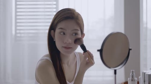 Woman Applying Makeup in Front of Mirror
