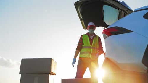 Zusteller im Außendienst im Overall belädt versiegelte Kartons mit Produktkäufen im Kofferraum