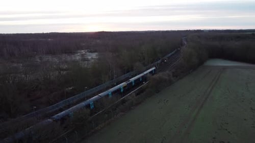 Drone footage of a train leaving the station with a sunrise in the background.