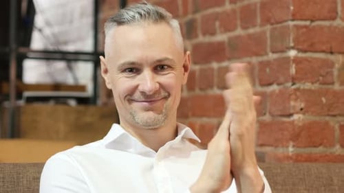 Man Smiling and Clapping Hands Sitting Indoors