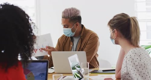 Man wearing face mask showing a document to his colleagues at office
