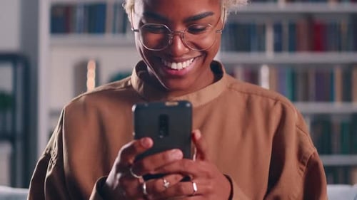 Young Adult Typing on Phone with Bookshelf