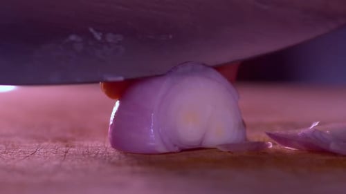Close up video of the hands of a man cutting thin slices of onion on a chopping board