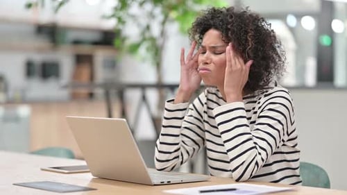 African Woman with Laptop Having Headache in Office
