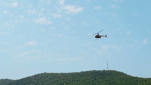 Helicopter Flying in Blue Sky Over Green Hill