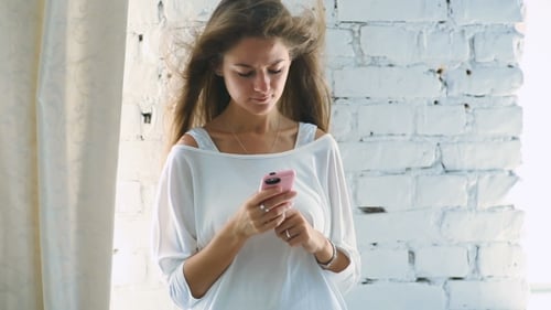 Woman Using Mobile Phone by a Brick Wall