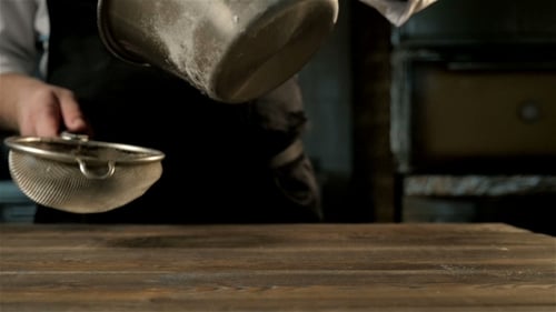 Chef sifts flour on a wooden table