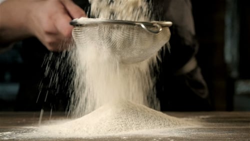 Chef Sieving White Flour onto Wooden Table