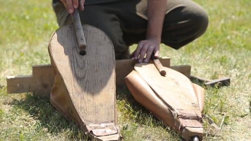 Man demonstrates bellows for blacksmithing on green grass