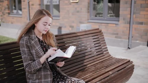 Young Woman Reading a Book on a Bench