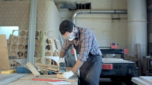 Bearded Carpenter In Safety Glasses Working With Electric Planer In Workshop