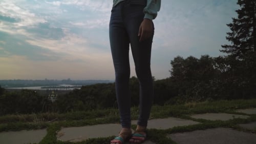 A Girl In a Light Jacket And Standing In The Yard Talking On The Phone.