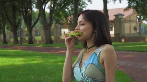 Girl Sitting On The Ground In The Park And Eating a Sandwich.