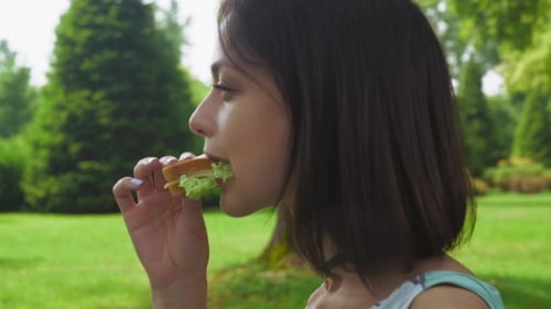 Girl Brunette Sitting In The Park And Eat a Sandwich With Salad. .