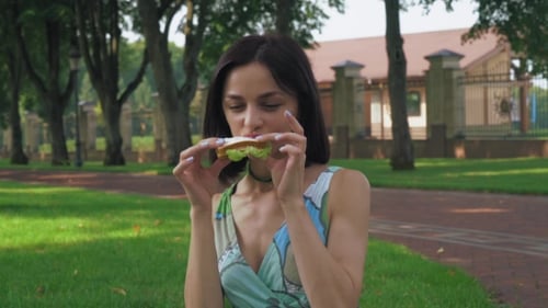 Attractive Brunette Girl Eating a Sandwich In The Park.