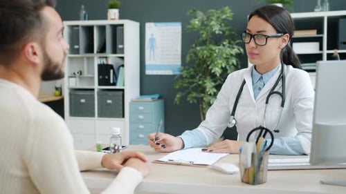 Female Medic Consulting Unhealthy Man in Hospital Office Talking Writing in Medical Records