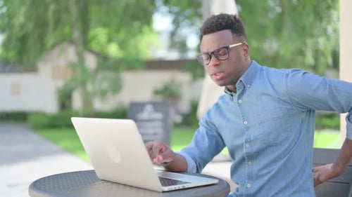 Young Adult Working on Laptop Outdoors With Back Pain