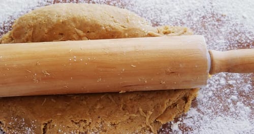 Rolling Pin Flattening Dough with Flour on Wood