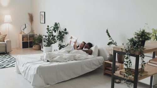 LGBTQ Couple with Tablet Lying in Bed in Cozy Apartment