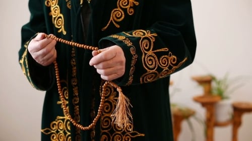 Un vieux mollah en costume national priant avec des perles de chapelet à la main