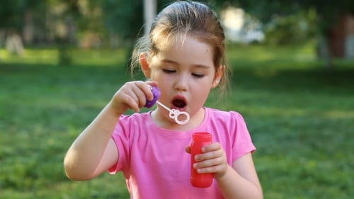 Happy Child Blowing Soap Bubbles In Park