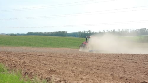 An Agricultural Tractor Plowing a Field. Hills And a Forest At The Background. Soil Dust All Over