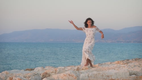 Woman Dancing on Rocky Beach at Sunset