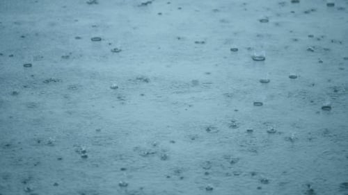 Rain Drops Rippling In a Puddle With Blue Sky Reflection