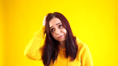 Close Up of Young Woman Scratching Thoughtfully Her Head on Yellow Background