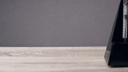 Un métronome vintage noir bat le rythme debout sur la table, derrière un fond gris