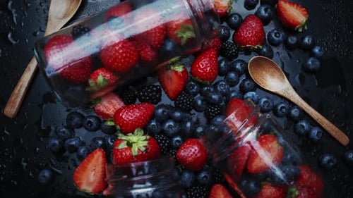 Cuisson de la confiture de framboises et de myrtilles. Déposer dans un bocal en verre. Rotation sur fond noir