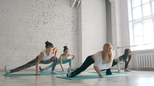 Women Exercising and Stretching in Bright Yoga Studio