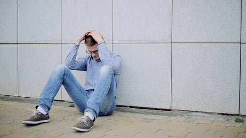 Young Adult Man Sitting Anguished Against Wall