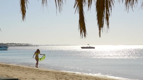 Woman Walks on Sunny Beach with Green Scarf