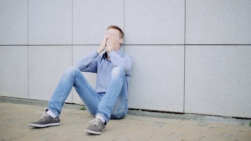 Frustrated Young Man Sitting With Back Against Wall